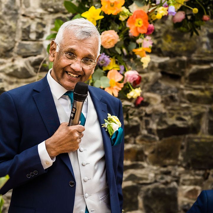 Brides father gives speech in front of colourful floral arch 