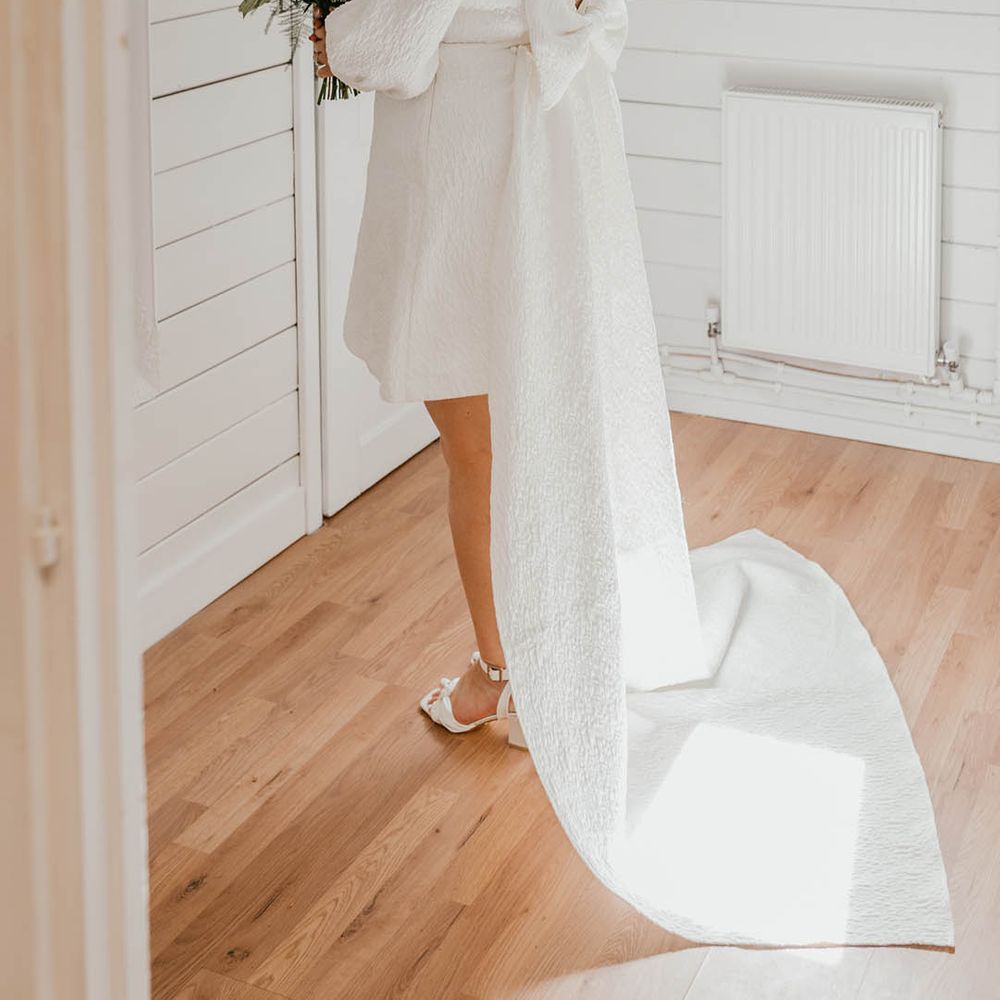 Bride in a short wedding dress with bow detail with her hair in a half up half down hairstyle with shoulder length veil 