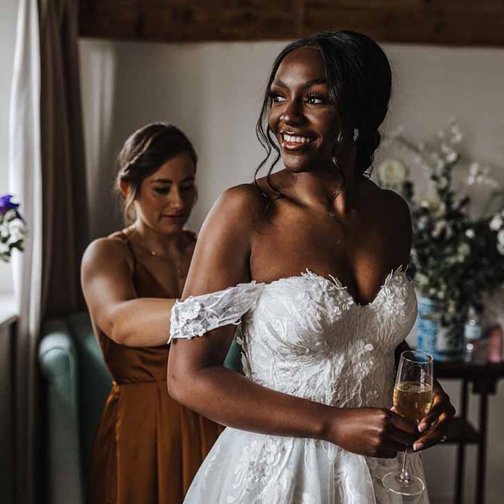 Bridesmaid in burnt orange bridesmaid dress helping bride with bridal preparations in her sweetheart neckline lace wedding dress with detachable off the shoulder sleeves 