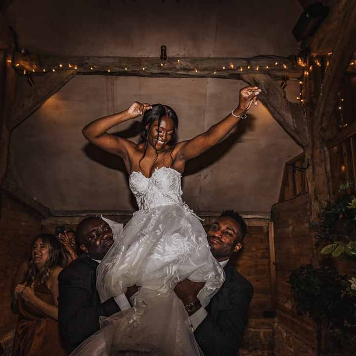 Bride in sweetheart neckline lace wedding dress being lifted up by groomsmen during wedding disco 