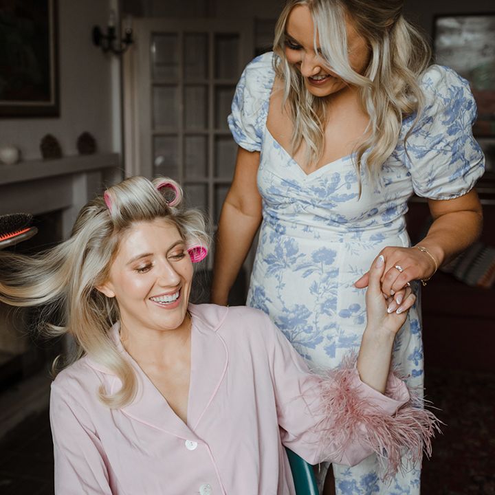 Bride in pink pyjamas with pink feather cuff detail gets her hair done for the wedding day 
