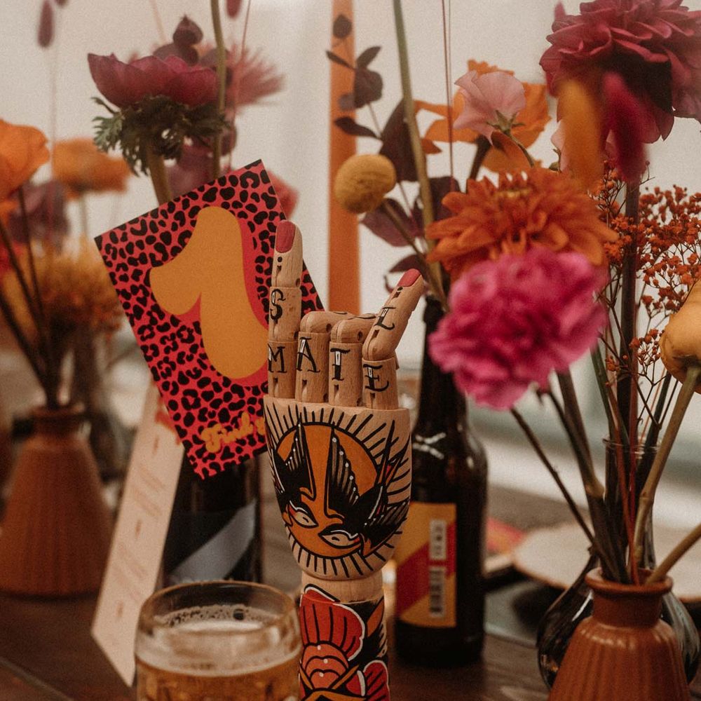 Eclectic rustic wedding tablescape with wooden hand with tattoo paintings, leopard print wedding table number and vibrant floral centrepieces 