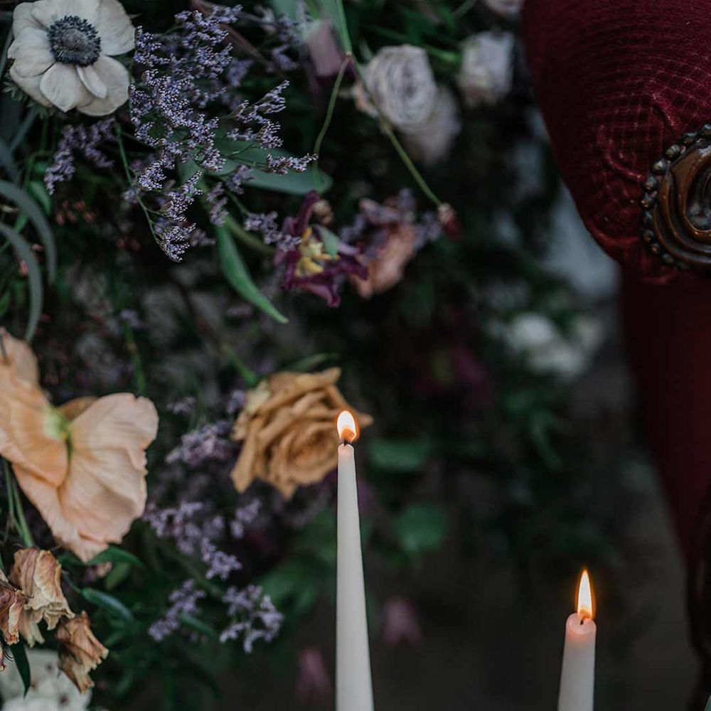 Neutral tapered candles in gold candlesticks surrounded by suspended wildflower and foliage arrangements in large gold vases at Buxted Park