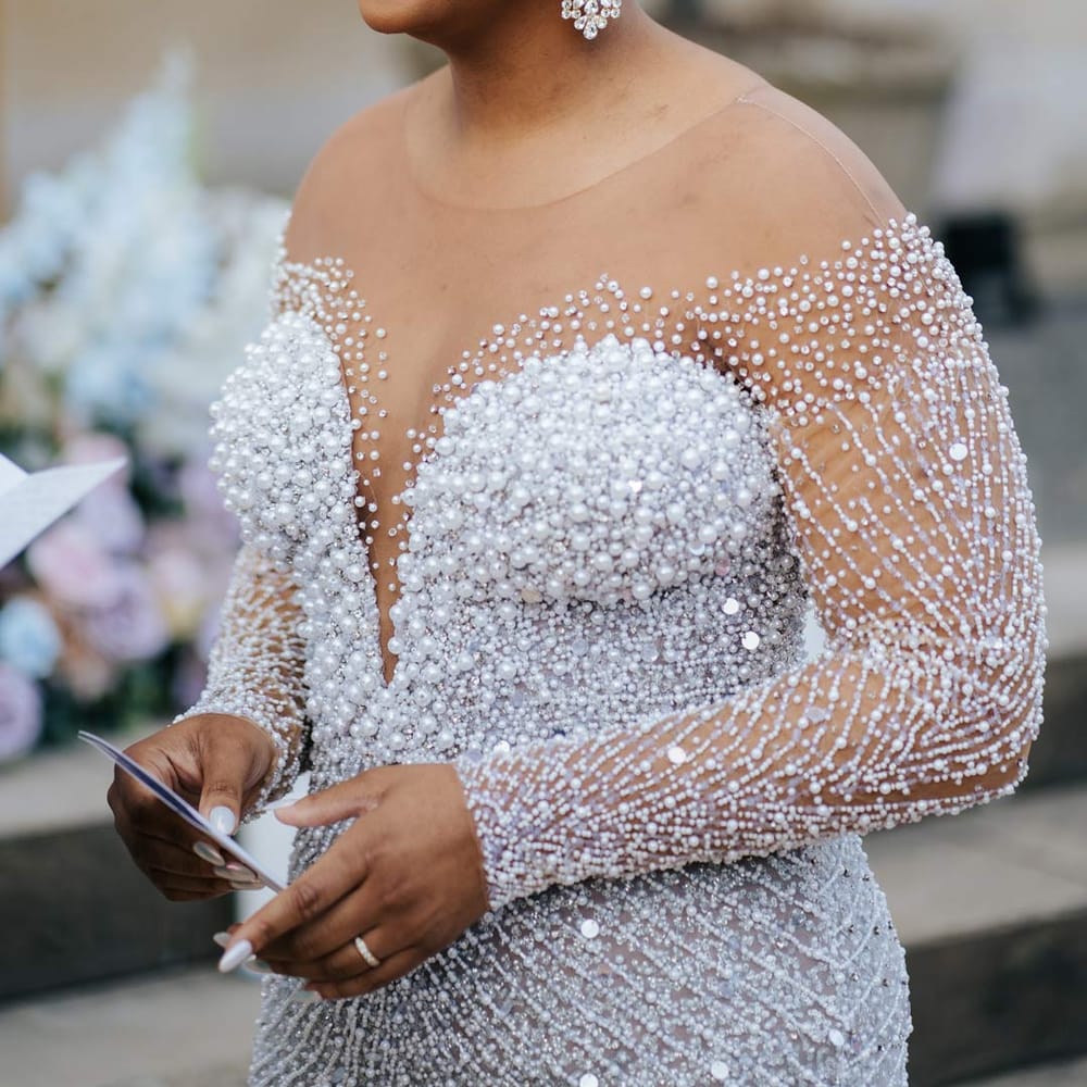 Bride reading her vow renewal wearing illusion v neck sheer off shoulder long sleeve pearl embellished wedding gown at outdoor ceremony at Syon Park