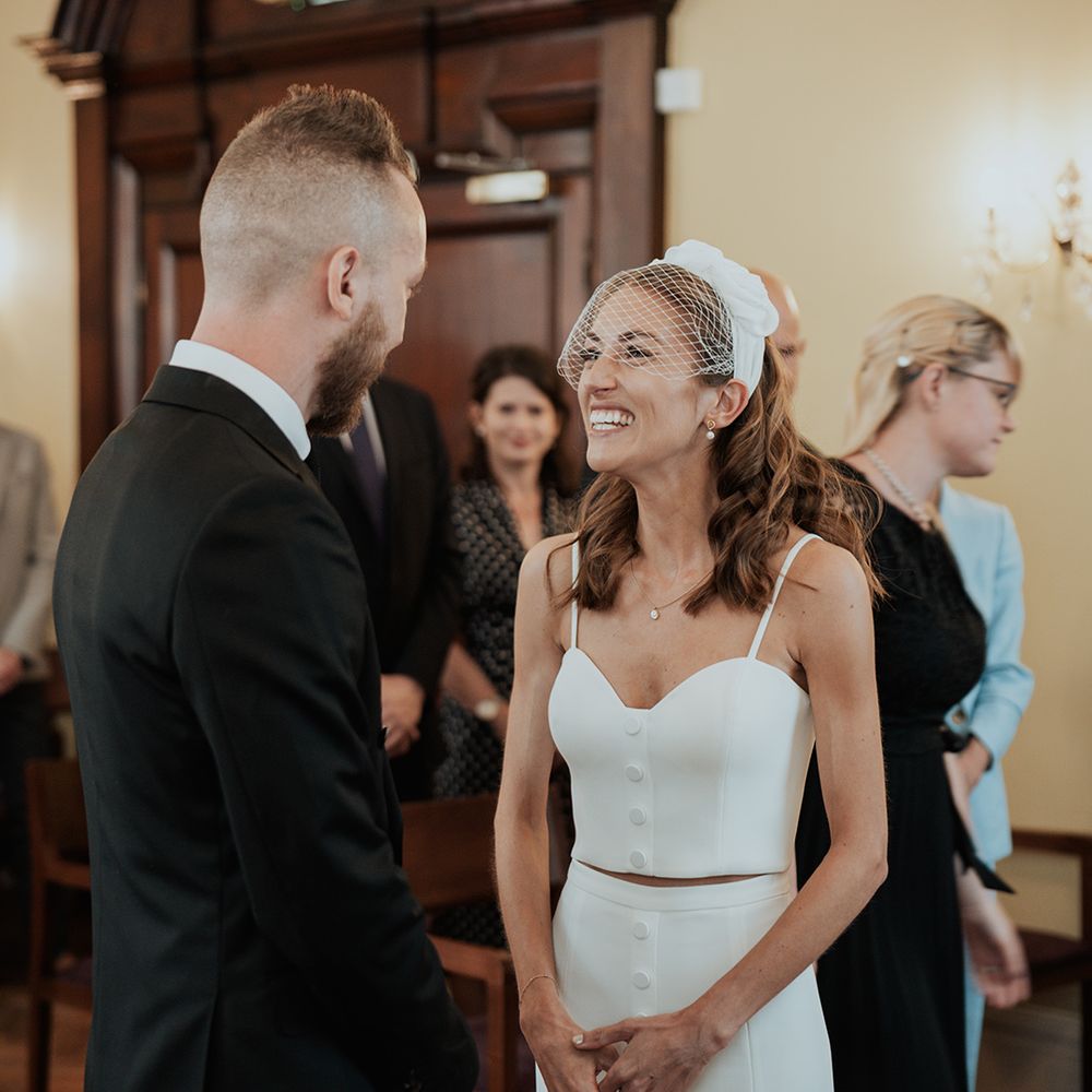 bride in bridal separates and a birdcage veil smiling during the Chelsea registry office wedding ceremony 