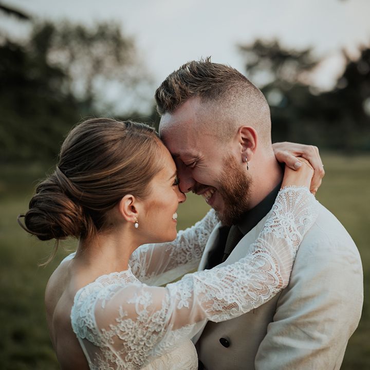 bride with a low bridal bun and lace long sleeve wedding dress embracing her groom in a beige wedding suit