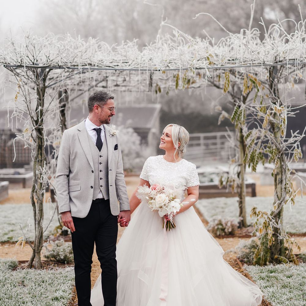 The groom in a light grey suit walks along with the bride in an embellished top and princess tulle skirt 