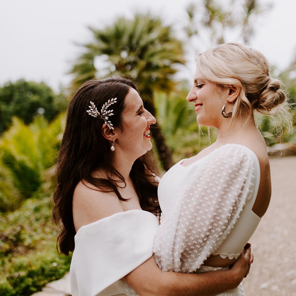 Bride with side swept hair and pearl hair accessory embracing bride in two piece top and skirt 