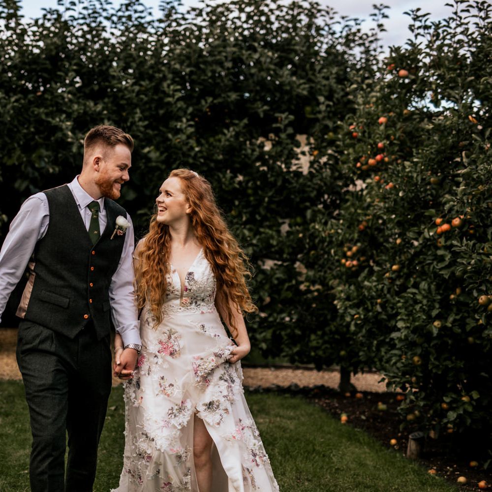 Bride & groom walk through gardens holding hands