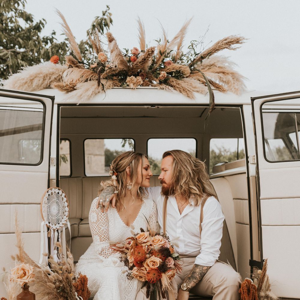 Bride & groom sit outside Camper Van with floral decoration 