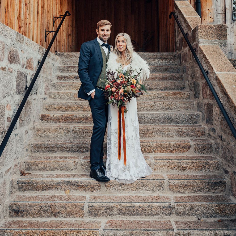 Bride & groom pose together on steps whilst bride wears feathered shawl
