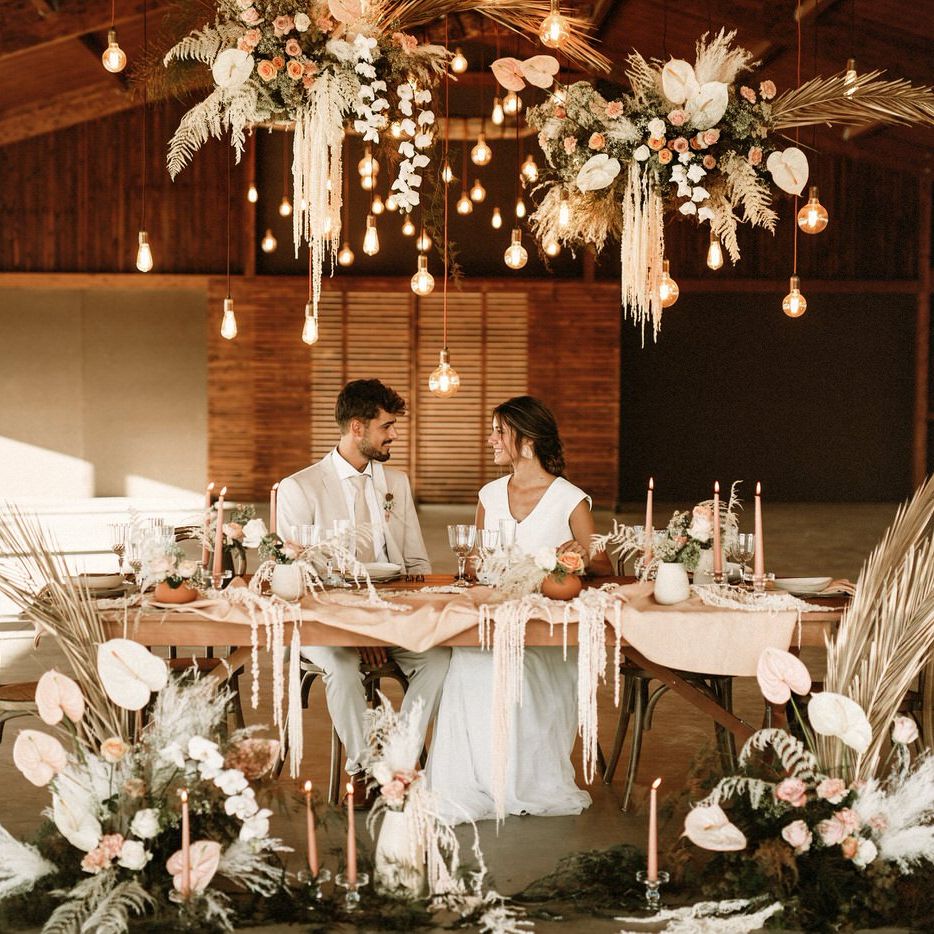 Bride and groom sitting at an intimate tablescape filled with dried flowers, taper candles, natural linens and coloured ceramics under a festoon light installation