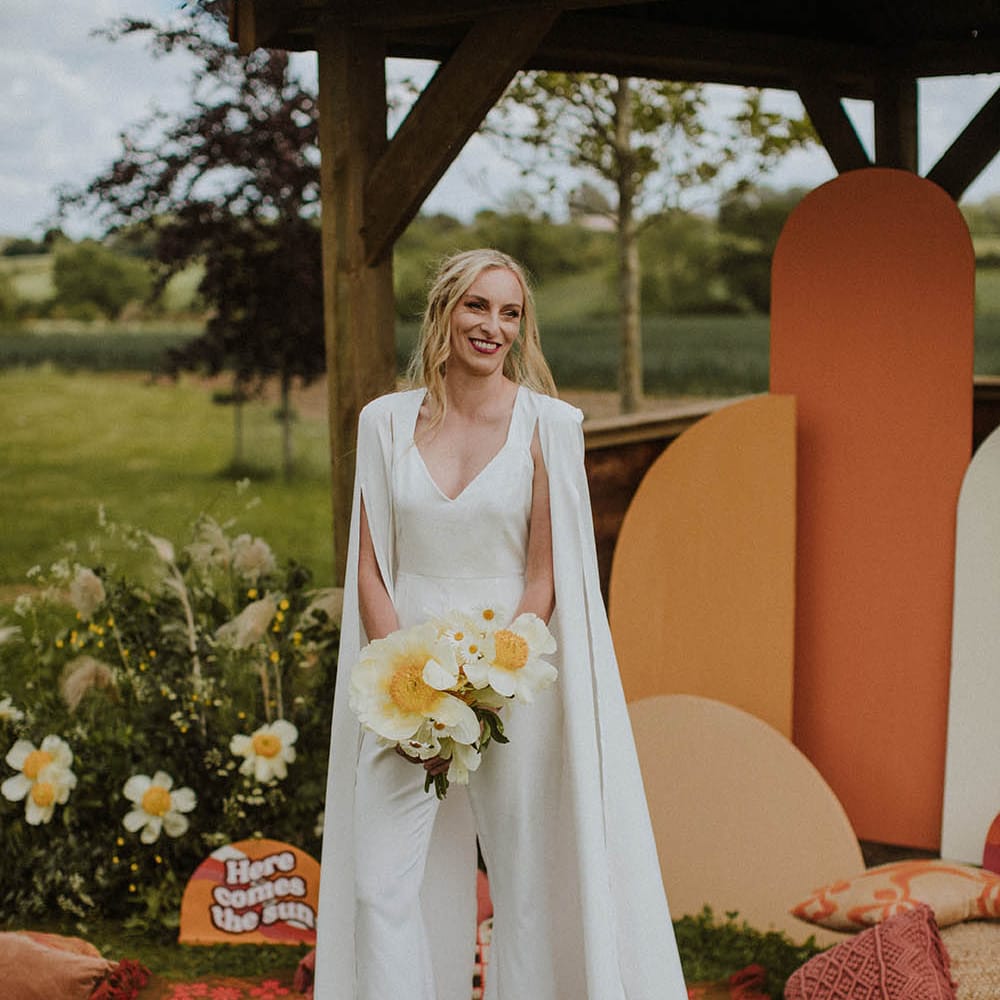 Stylish bride in a jumpsuit with cape and red velvet platform shoes 
