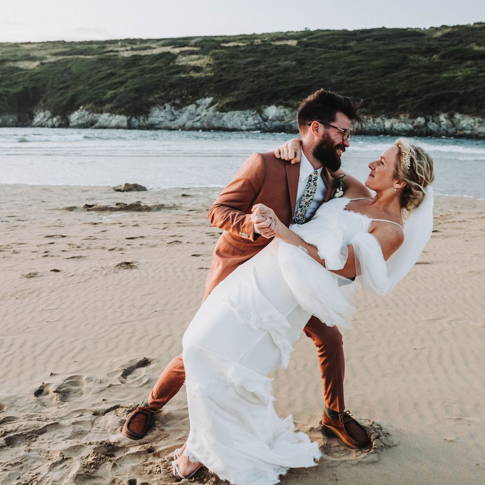 Groom leans his bride back on the beach in Cornwall on their wedding day
