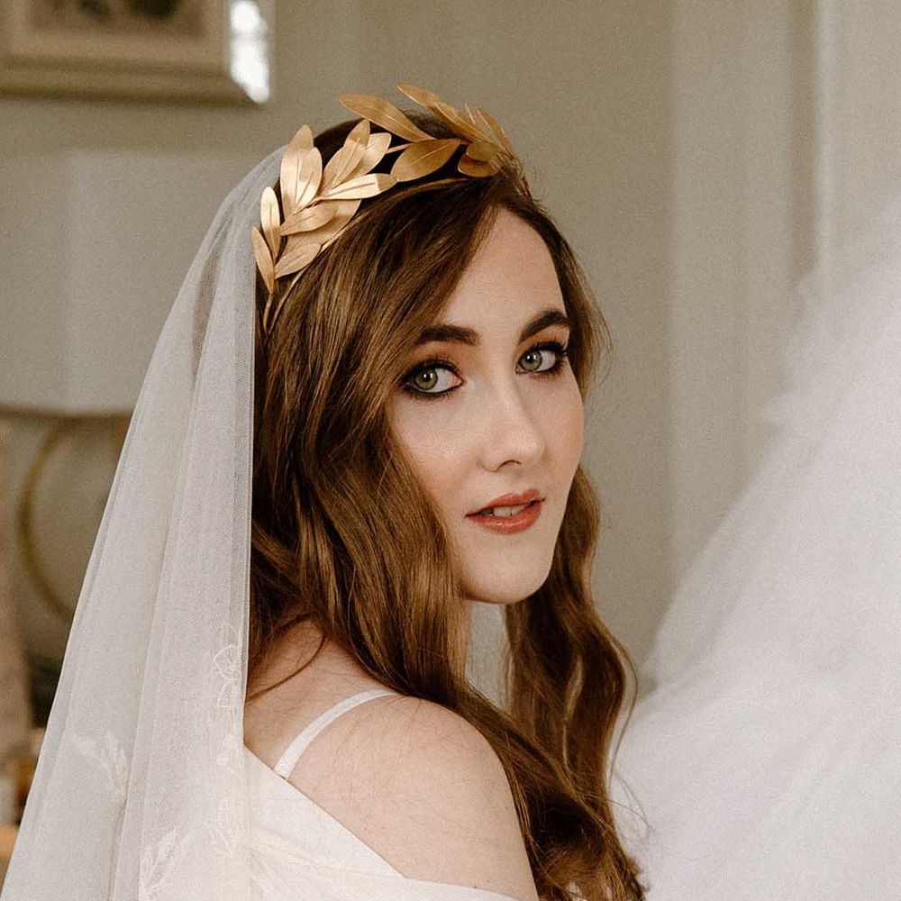 Beautiful bride with long wavy hair and eyeliner wearing a lace veil and gold laurel crown headdress