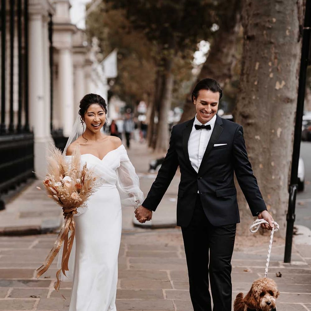 Bride and Groom smiling in Chelsea London in elegant wedding garments along side cockapoo dog 
