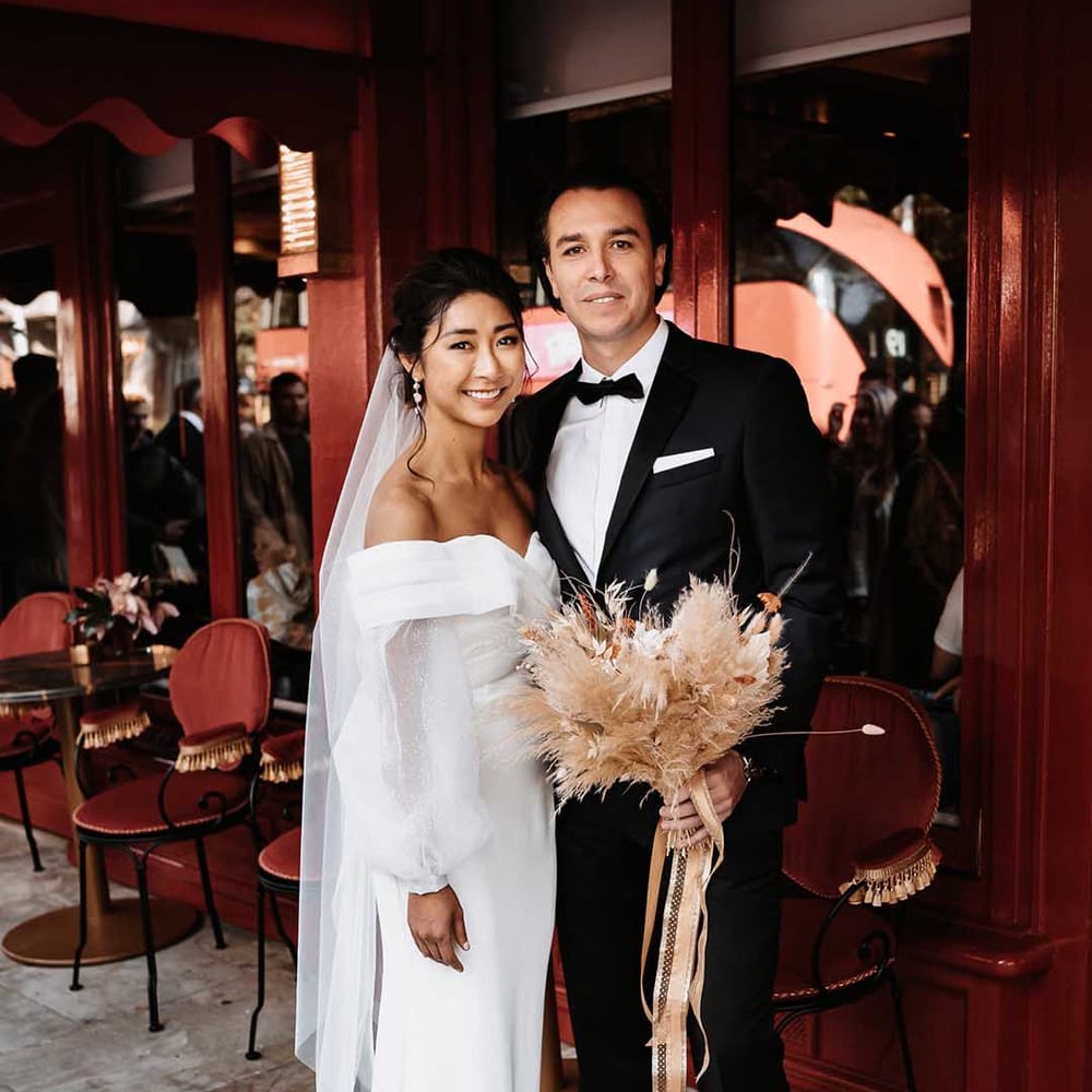 Bride wears Silky wedding dress and Groom is dressed in a black suit whilst holding a bouquet of bunny tails & mixed dried flowers