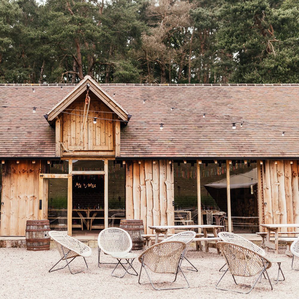 Wooden clad exterior of The Bridal Barn in Claverley for summer wedding with fairy lights and rattan garden chairs