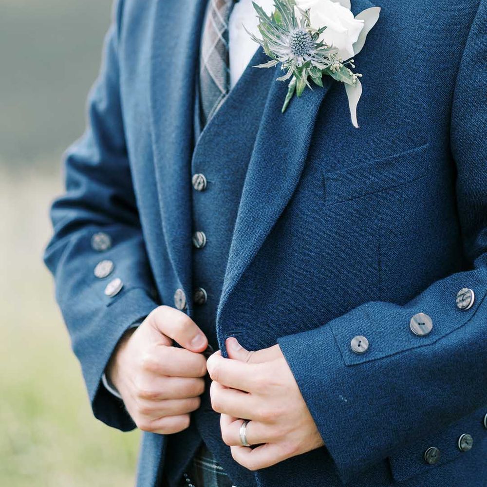 groom in a blue wool waistcoat and jacket with white rose buttonhole flower 
