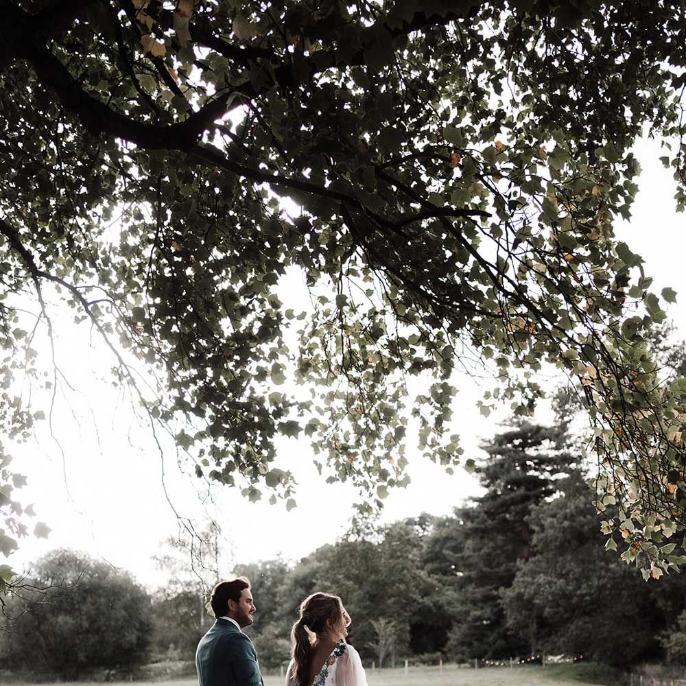Groom in blue suit walks with bride in low back wedding dress with train through grounds of Iscoyd Park