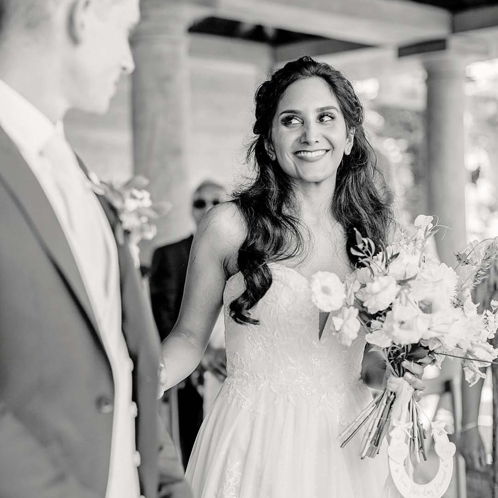 Indian bride wears her black hair in loose curls on her wedding day whilst holding floral bouquet 