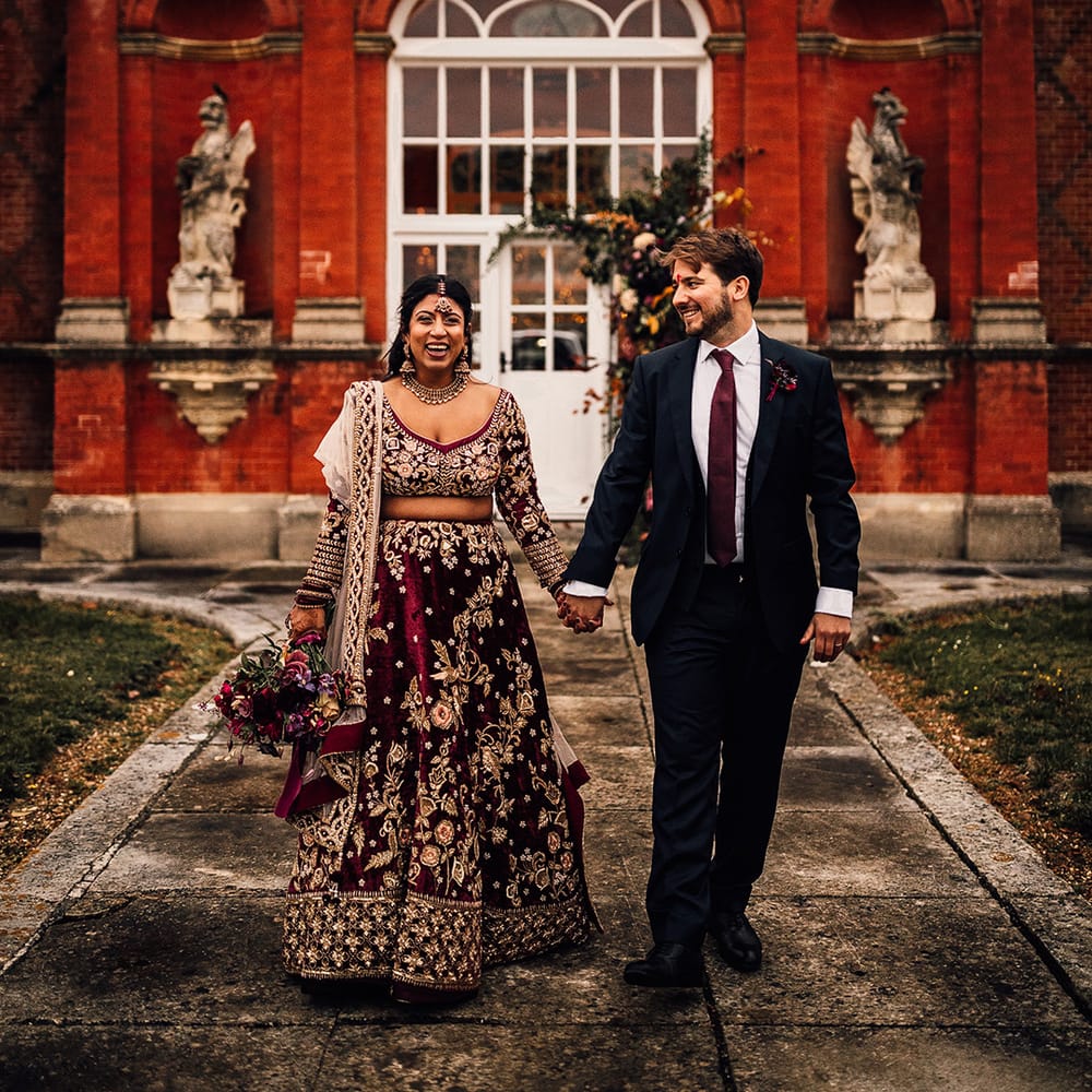 Groom & Bride match in their burgundy wedding outfits and smile at Minley Manor
