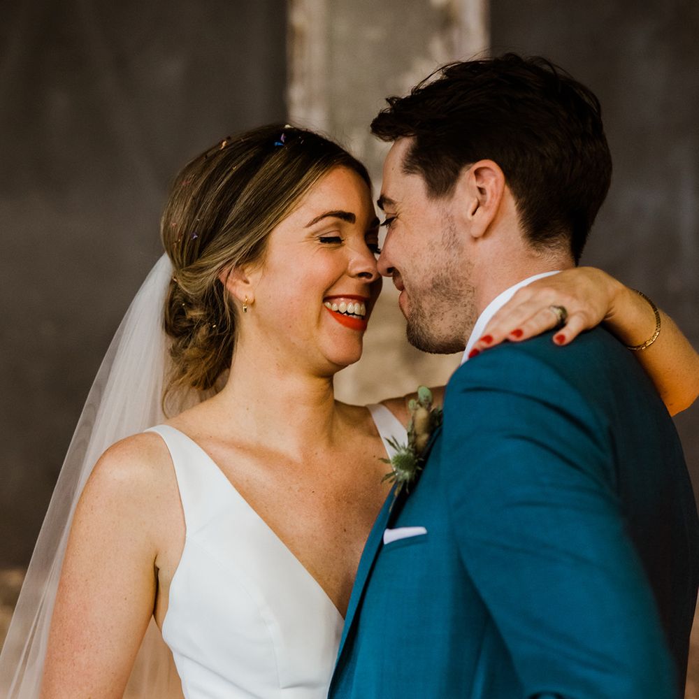 Bride in v neck wedding dress and groom in blue suit smile at each other