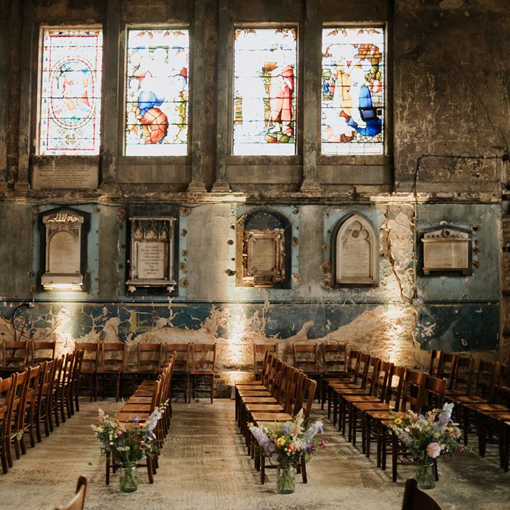 Asylum Chapel wedding venue with stained glass windows and brown wooden chairs for guests with wildflower decorations 
