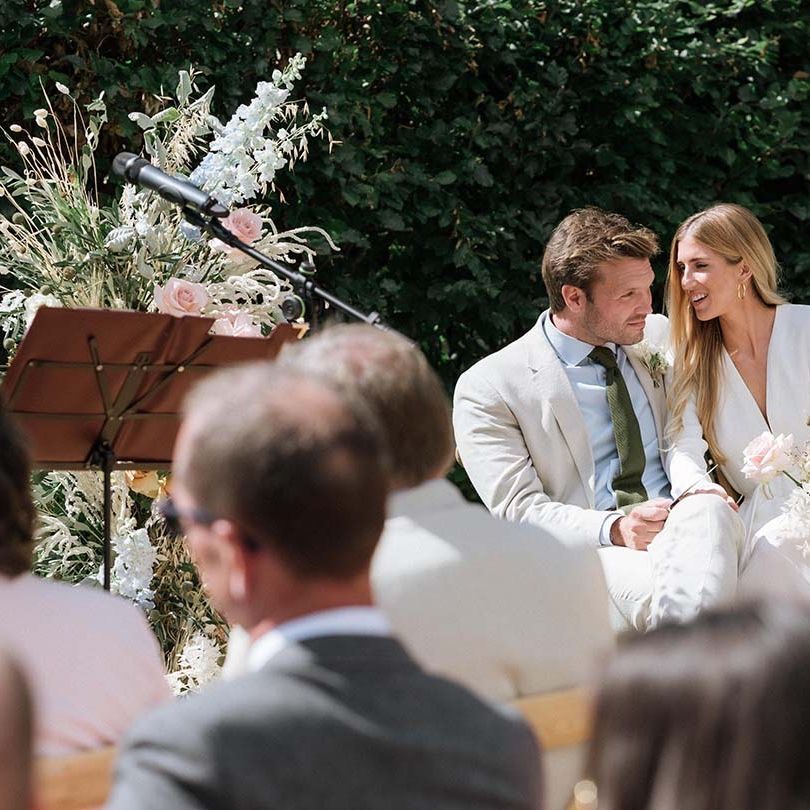 Bride and groom seated at their garden wedding in Bath with stunning pastel summer bouquets