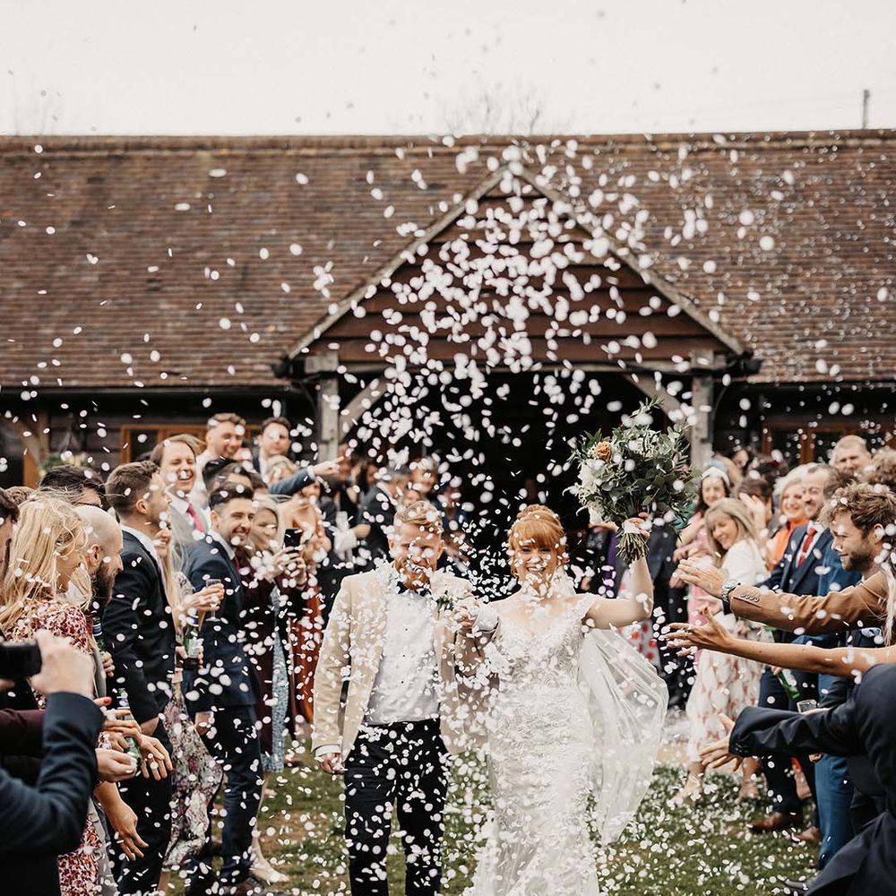 Bride and groom walk through confetti as they eke barn wedding venue on spring day 