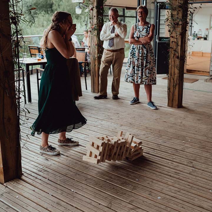 Wedding guests laugh as they play jenga on the deck of the cabin at lake wedding venue 