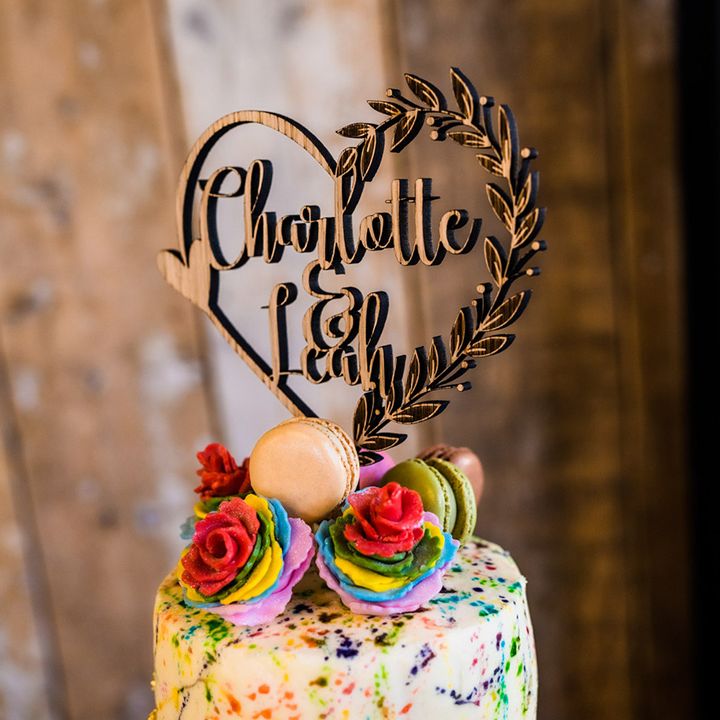 Wooden heart wedding cake topper with the couples' names and rainbow icing roses and macarons