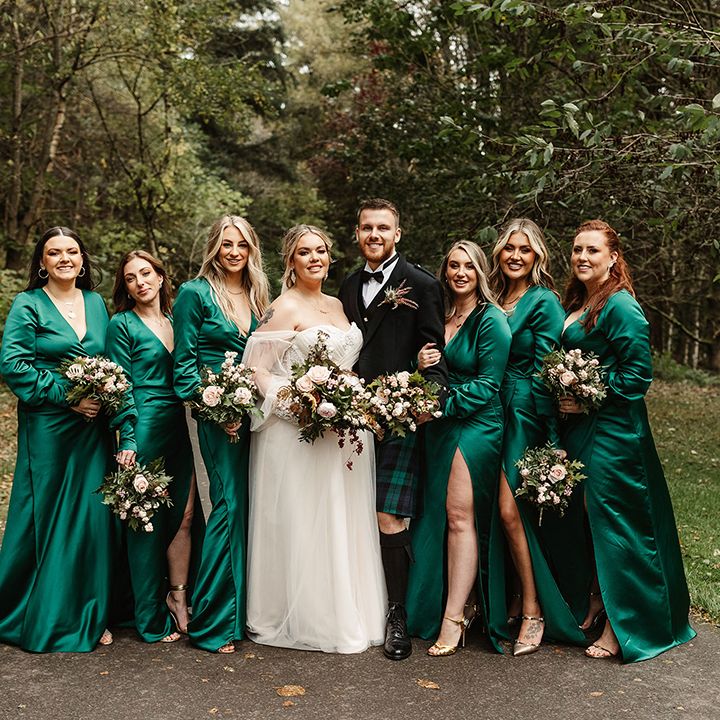 Bridal party with bridesmaids in emerald green v neck long sleeve front slit dresses with bride and bridesman 