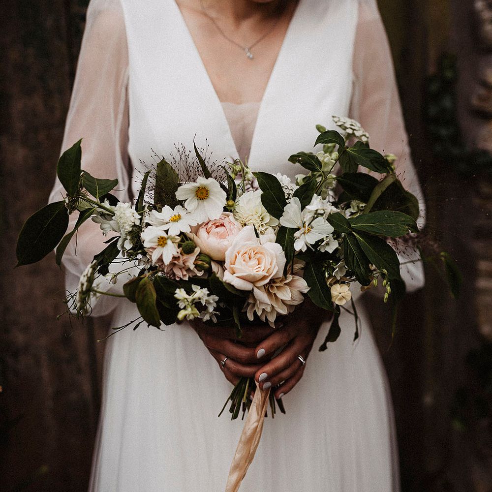 Pink roses, dahlias and white cosmos make up bride's wedding bouquet held by bride 