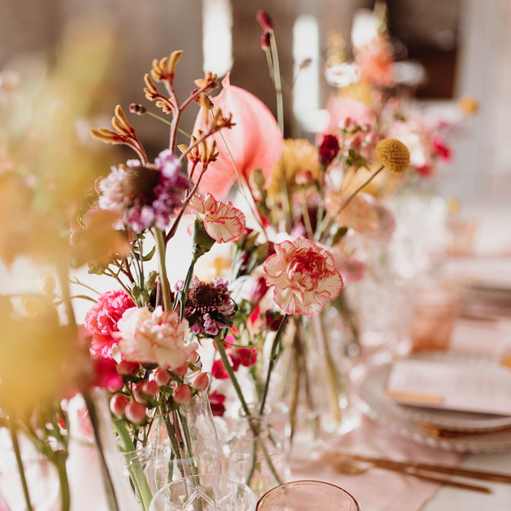 Wedding table centrepiece deco with pink and yellow carnations and billy button flower stems in bottles 