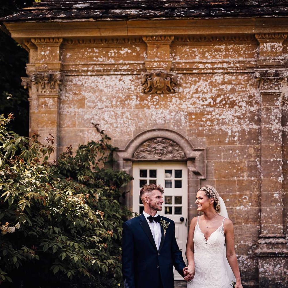 Bride and groom gaze at each other as they walk around their country house venue, Athelhampton House, together 