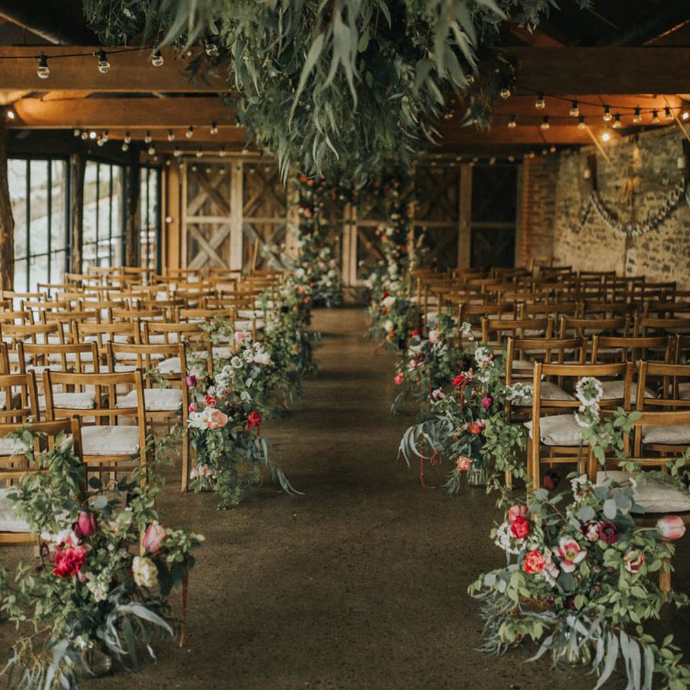 Wedding ceremony decor with crops hanging from the ceiling and flowers lining the aisle at Dewsall Court 