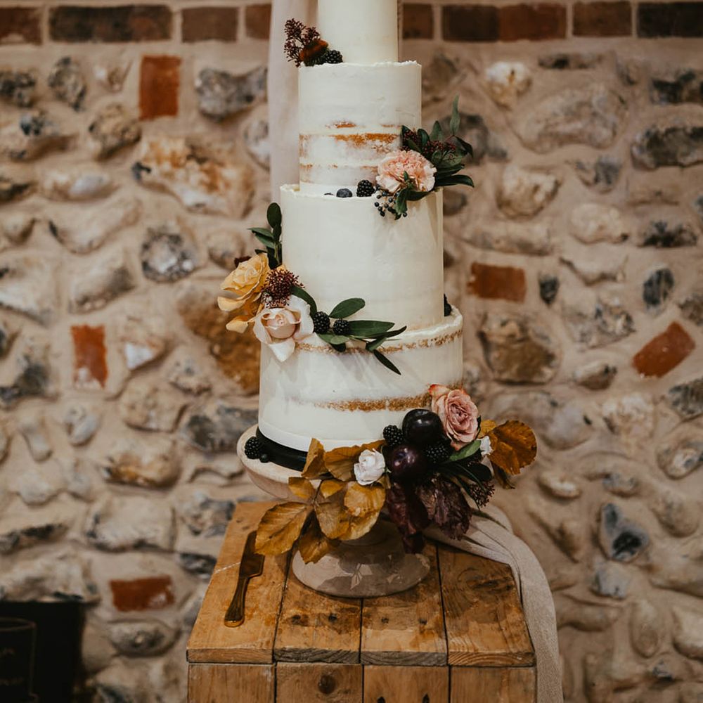 Four tie rustic wedding cake with white frosting with autumnal flowers and a personalised cake topper 