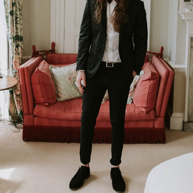 Groom with long hair tied up in a black suit with bow tie 