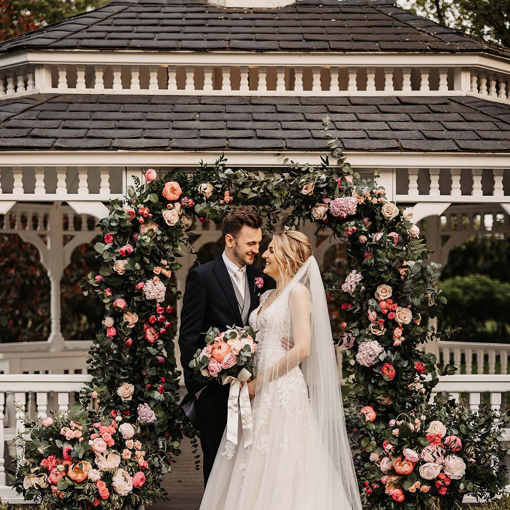Bride and groom share an embrace in front of their pink flower arch altar decoration 