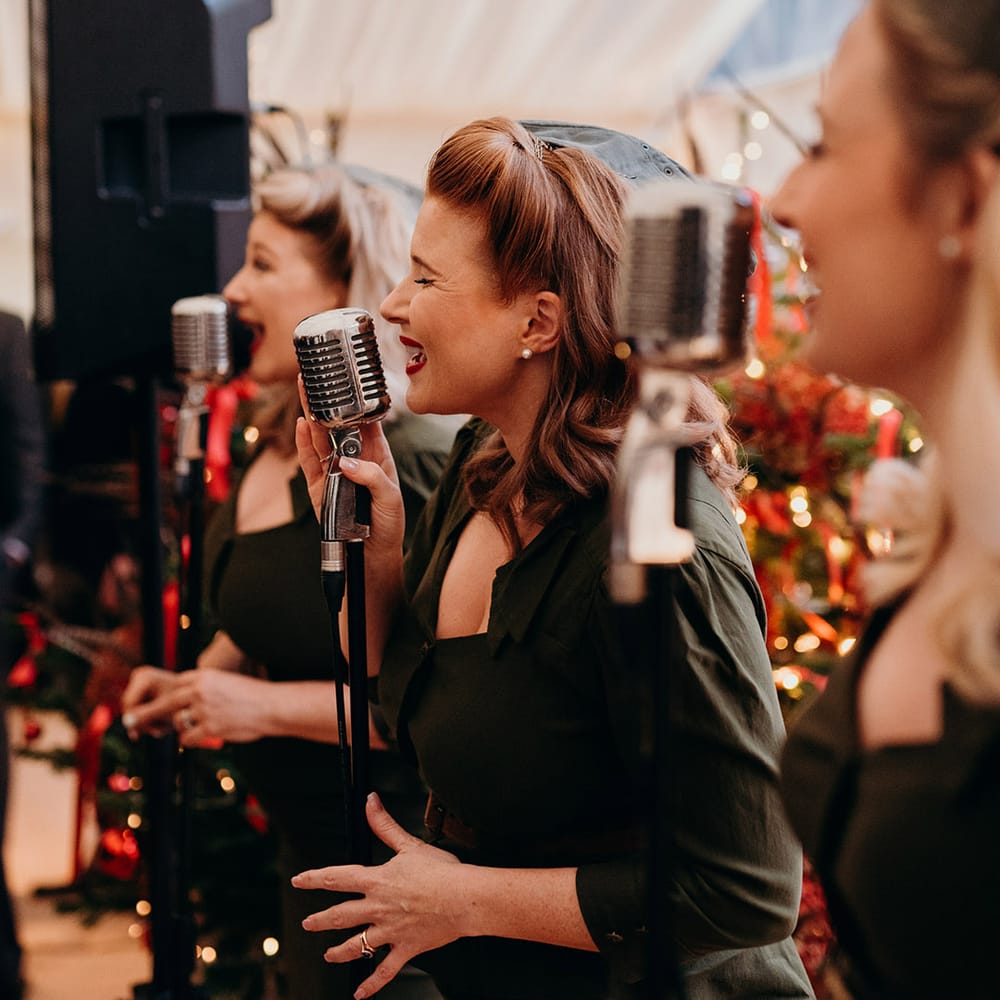Singers in vintage clothing with sweetheart necklines and red lipstick singing at Christmas wedding
