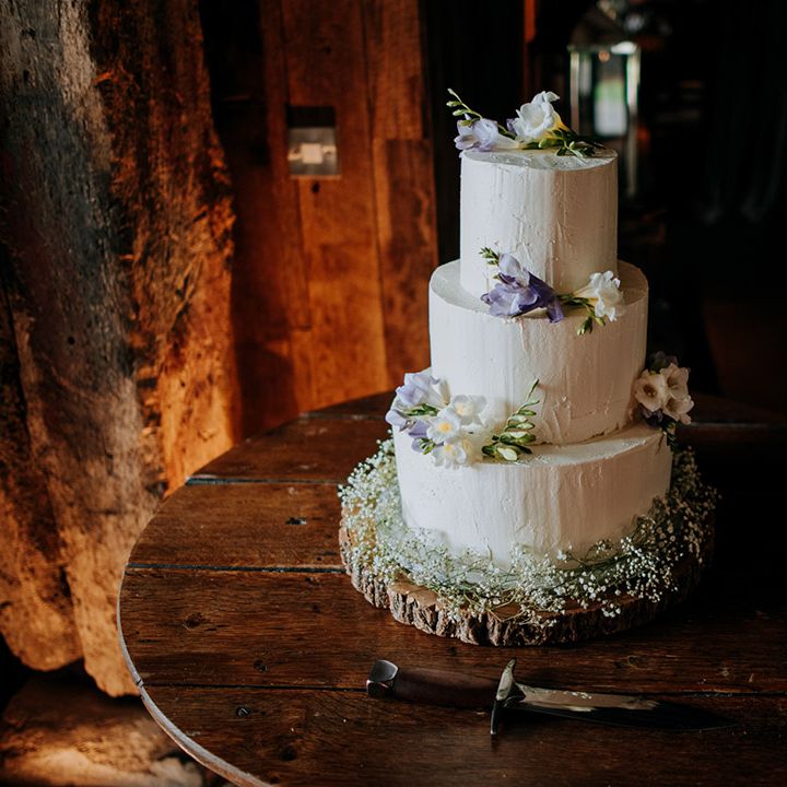 Three tier white frosted wedding cake complete with colourful floral decor on wooden block
