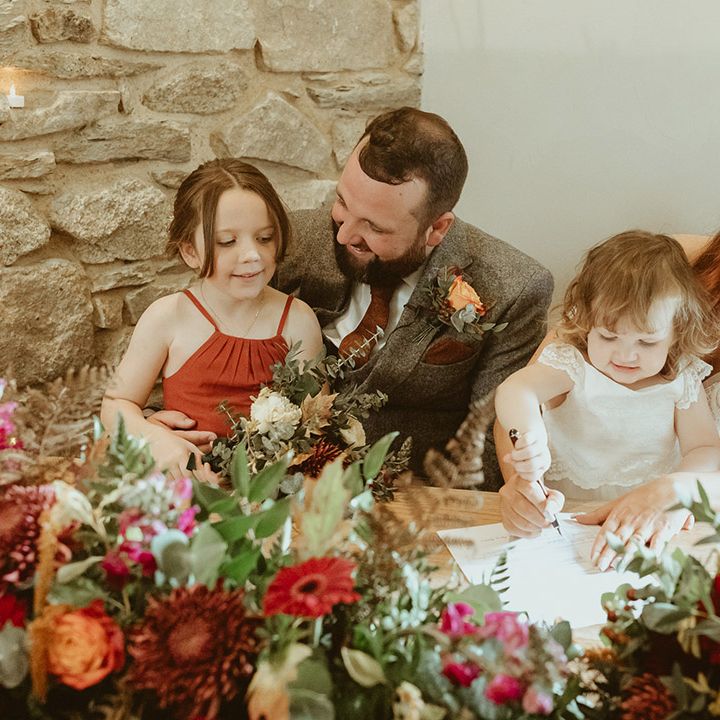 Bride and groom sign the wedding register with their daughters for autumn wedding 