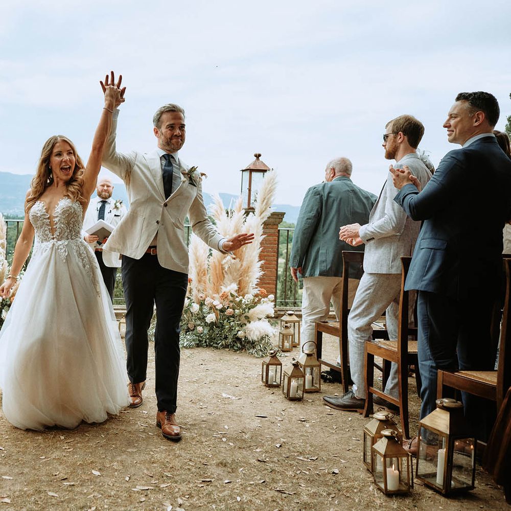 Bride in embroidered tulle wedding dress walking out of ceremony with groom in linen suit and cheering
