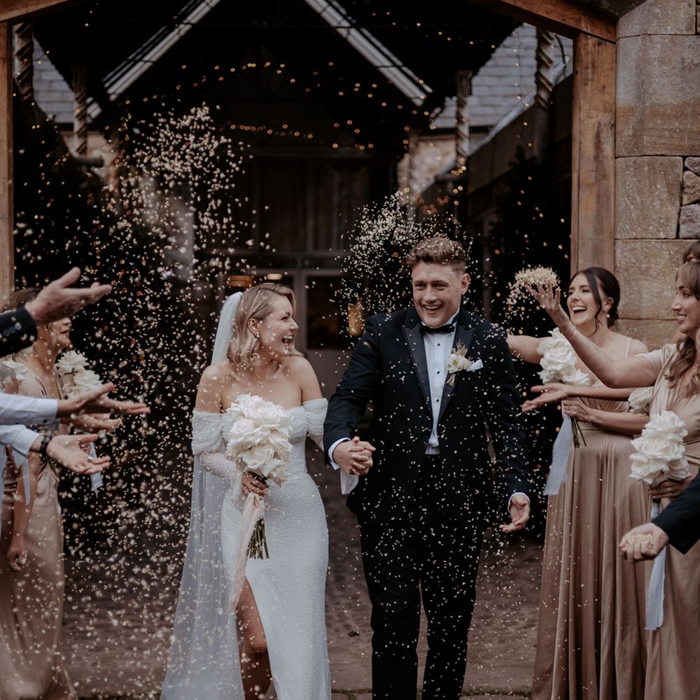 Fun confetti moment for the bride and groom in black tie as they exit from their bespoke wedding ceremony as a married couple 