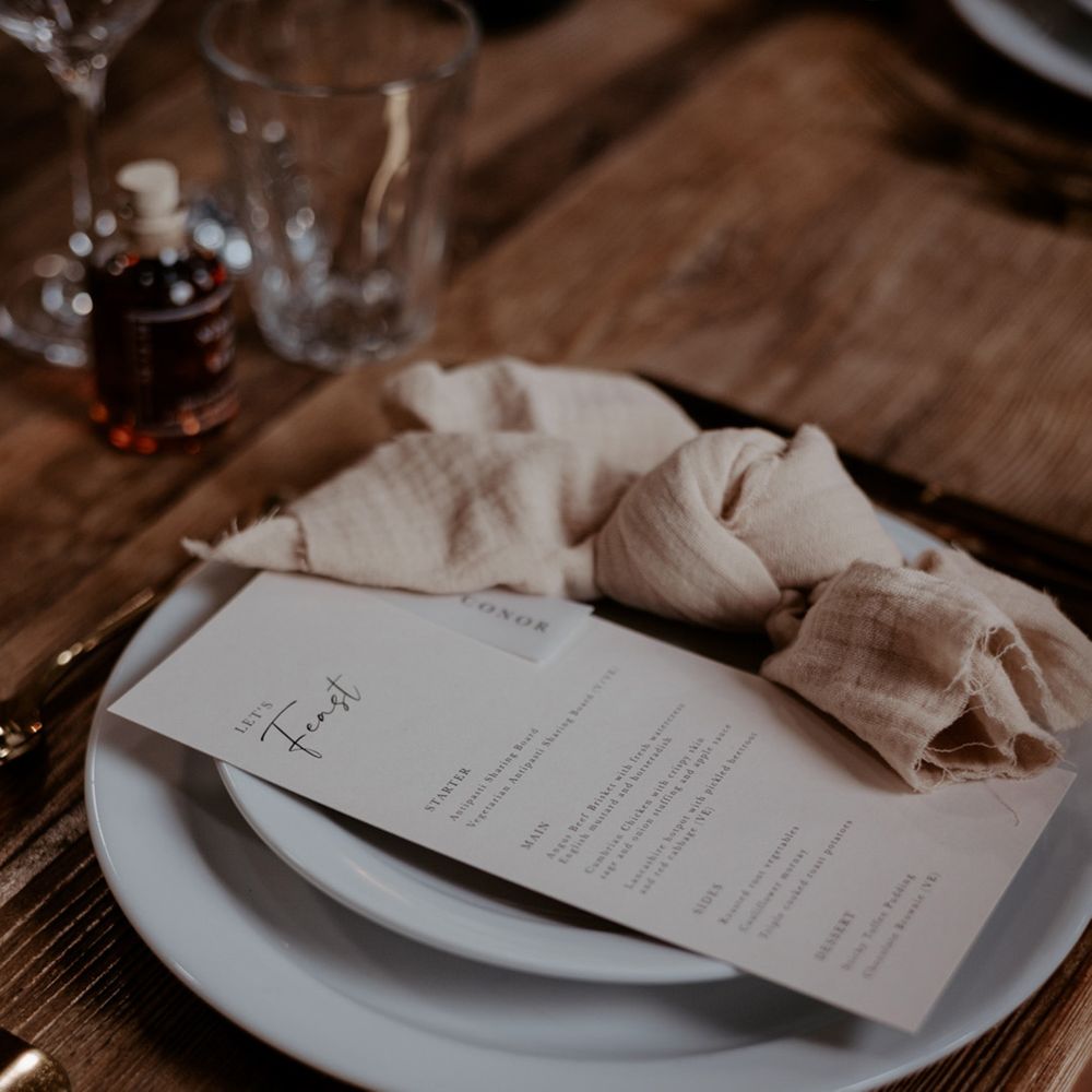 Minimal and simple wedding place setting with white plates, a neutral wedding napkin and neutral wedding menu card 