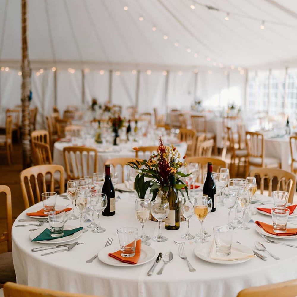 Classic wedding tablescape with dried orange and yellow flower and foliage wedding centrepieces on wooden tree trump circles in wedding marquee with fairy lights and festoon lighting