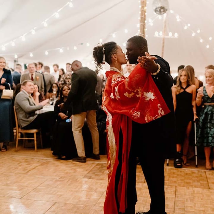 Bride in traditional red and gold Chinese silk kimono doing wedding first dance with groom in navy Nigerian traditional wedding outfit at Broadfield Court