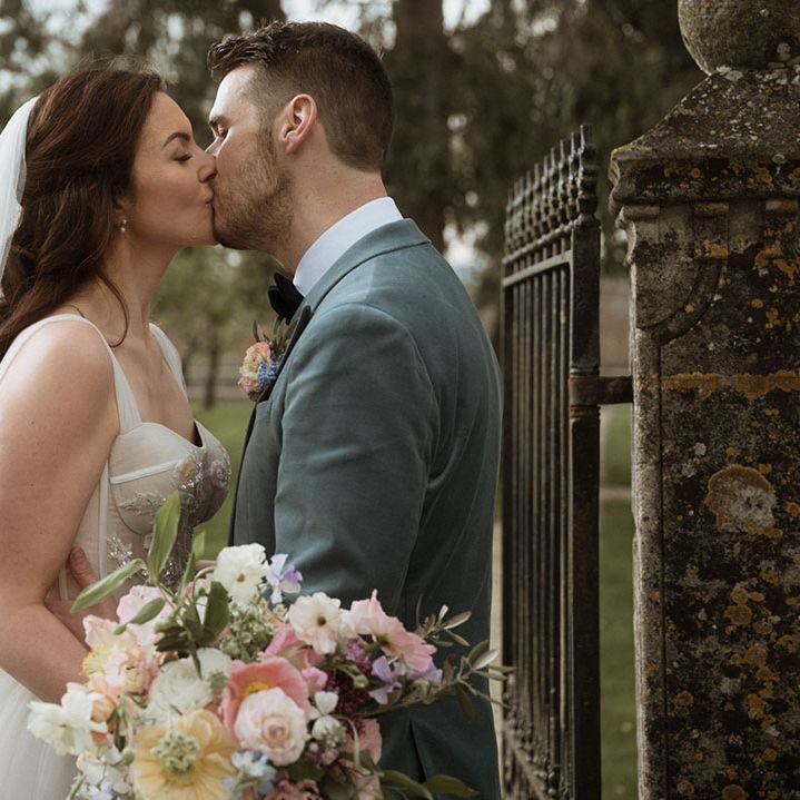 The groom in a powder blue velvet blazer kisses the bride for their cute couple wedding portraits 