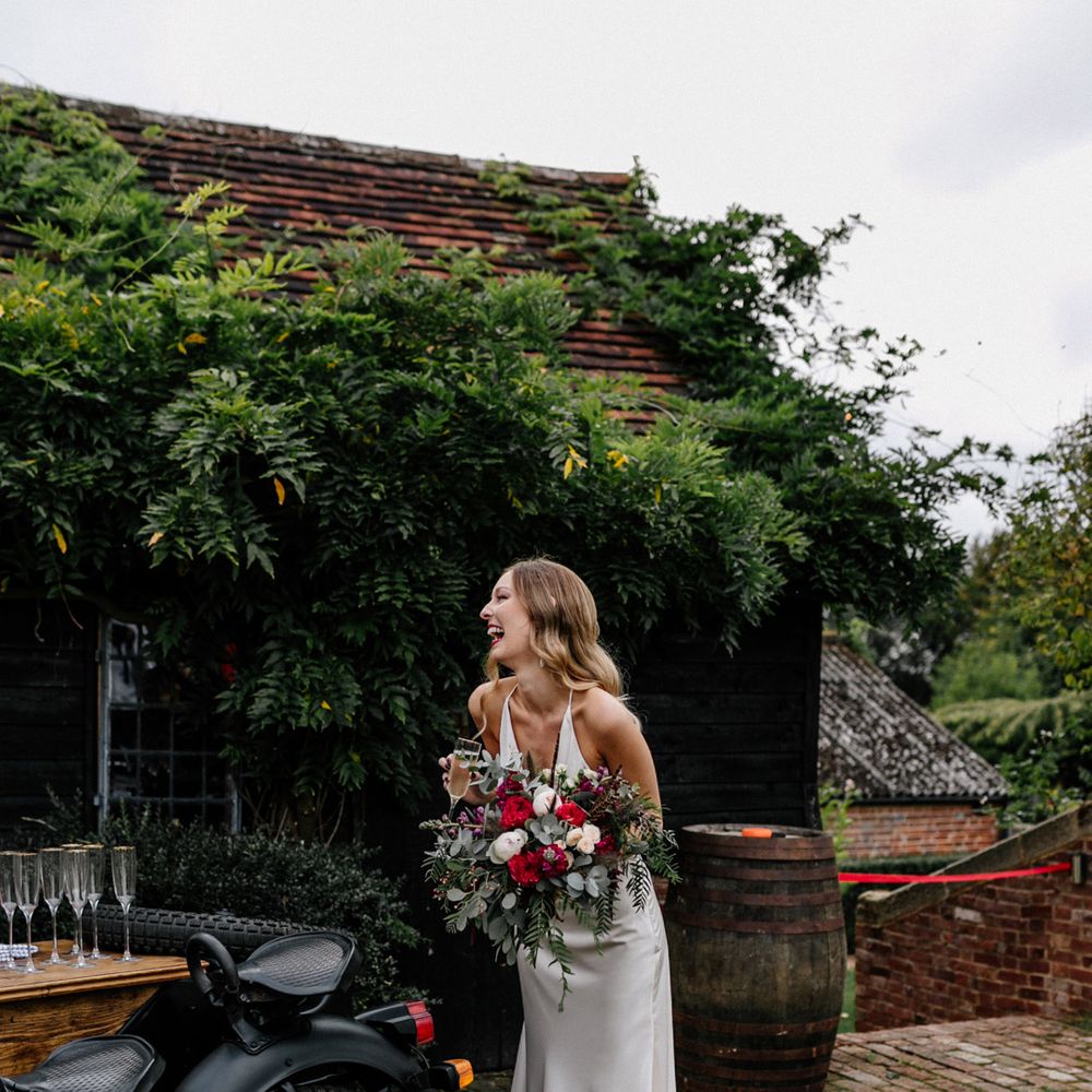 Bride in satin wedding dress standing next to a motorcycle prosecco bar
